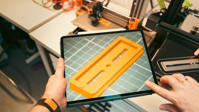 Handwerker hält ein Tablet mit 3D-Modell vor einem 3D-Drucker in der Werkstatt