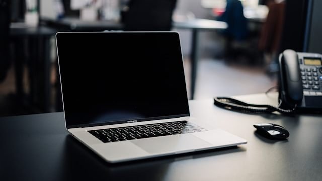 Aufgeklappter Laptop auf einem Bürotisch, daneben ein Festnetztelefon