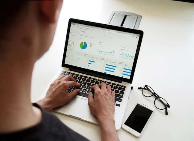 Person arbeitet konzentriert am Laptop mit Analyse-Dashboard, Smartphone und Brille daneben